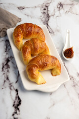 Fresh sweet and salty golden butter croissants alone and filled with ham and cheese on white sheet