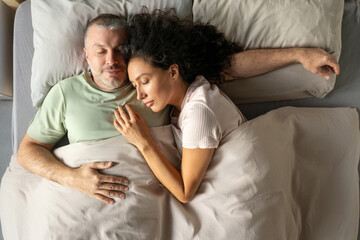 Happy husband and wife sleeping in hug on bed, enjoy good cozy morning together in bedroom...