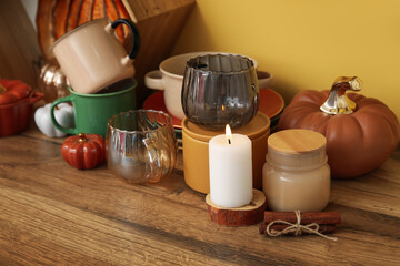 Different dishes, autumn decor and burning candle on wooden table in kitchen