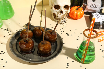 Plate with tasty caramel apples, cocktail and decorations for Halloween party on color table