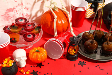 Sweet treats, plastic cups and decorations for Halloween party on red table