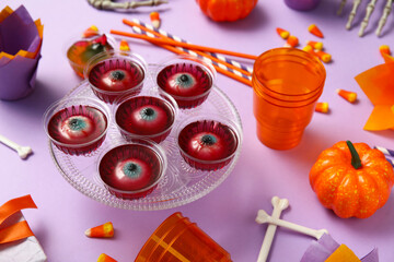 Composition with sweet treats, tableware and decorations for Halloween party on lilac background