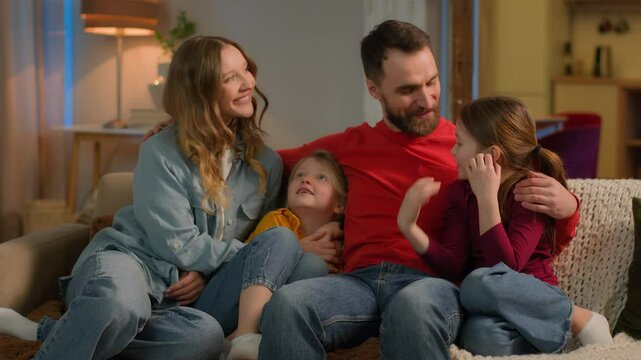 Happy friendly bonding affectionate family Caucasian parents children little girls daughters siblings on sofa evening weekend cheerful mother father kids hugging smile laugh relax home mortgage loan