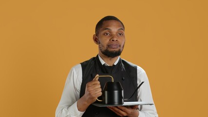 Restaurant staff serving clients with tea before their dinner order, bringing the teapot at the table. Waiter dressed in apron serves customers for satisfaction, service oriented industry. Camera A.