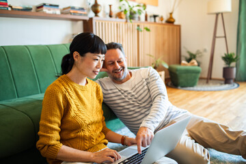 Couple using laptop together on the living room floor