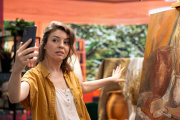 Female artist filming her finished rustic artwork for self promotion and marketing, presenting her masterpiece on social media audience. Advertising painting technique done with brush kit in studio.