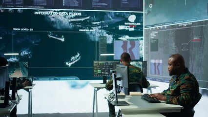 Military crew in a high tech operations command post managing information from radar cctv systems, real time data to support defense missions. Army protocols for national security. Camera B.