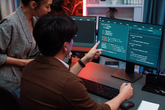 IT developers discussing with point to intelligent website development coder system running data online two screens information technology at neon light room at modern office. Infobahn.