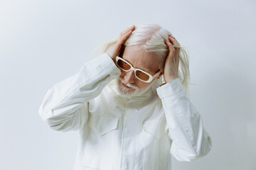 Elderly person with white hair and glasses touching their head, dressed in a white outfit,...
