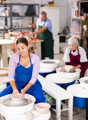 Young woman learning how to create pottery on potter wheel in a workshop