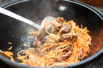 Pieces of lamb with carrots and onions are fried in boiling oil on the fire. preparation of traditional pilaf. cooking pilaf in a cast iron cauldron.