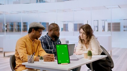 Businessman discussing with the real estate agents next to chroma key on tablet, meeting to negotiate leasing contract terms before looking at blueprints for an office relocation. Camera A.