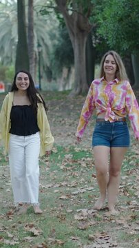 two young caucasian girls one brunette and one blonde walking barefoot on the grass towards the camera making thumbs up gestures and so-so gestures