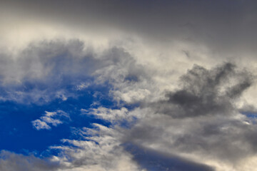 piece of a blue sky surrounded by white clouds with gray shadows.