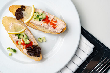 Tasty open-faced sandwiches with tuna spread, topped with fresh vegetables and lemon slices on a white plate