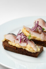 Open-faced sandwiches with herring and onions served on a white plate