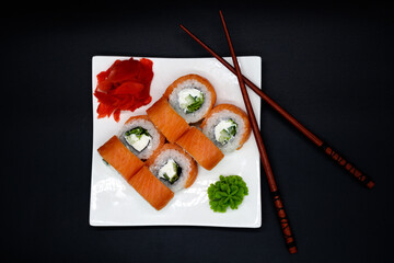 Prepared sushi rolls on a white plate on a black background