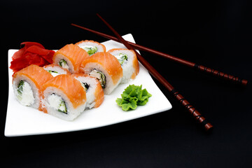 Prepared sushi rolls on a white plate on a black background