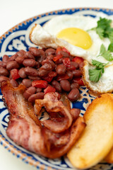 Delicious breakfast plate featuring eggs, beans, bacon, and potato wedges served on a decorative dish