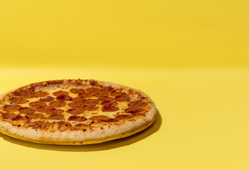 Pepperoni pizza off center on yellow background studio shot with copy space