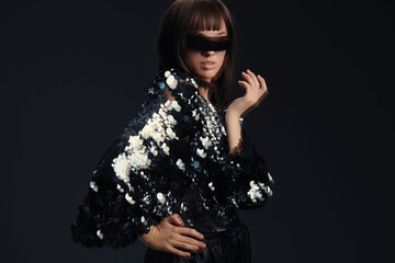 Woman, sunglasses, black sequinned jacket, dark background, hand on hip, eyes closed, confident pose a stylish woman in a black sequinned jacket and sunglasses, stands with her hand on her hip, eyes