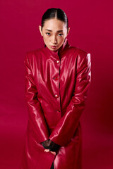 Fashionable asian brunette woman in a red leather coat striking a pose against a matching red background