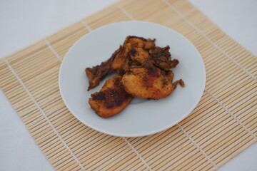 Fried chicken on a white plate with a bamboo mat