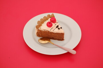 A piece of cake on a white plate with a spoon on a red background