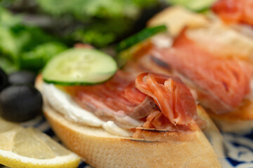Colorful plate of smoked salmon sandwiches with cucumbers, greens, and olives on a decorative blue platter