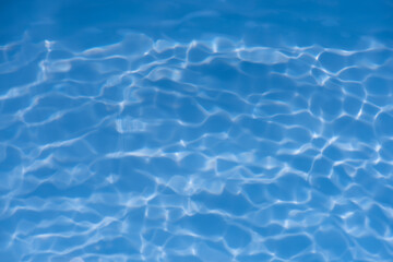 Blue water with ripples on the surface. Defocus blurred transparent blue colored clear calm water surface texture with splashes and bubbles. Water waves with shining pattern texture background.