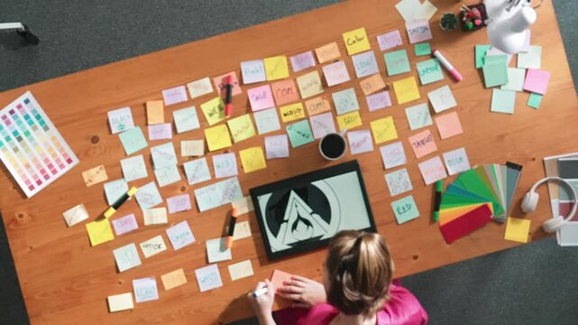 Top view of business team write graphic logo on meeting table with colorful sticky notes and design while explain idea. Project manager sharing idea and explain concept art to smart team. Symposium.