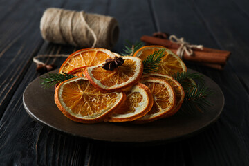 Dried orange slices on wooden plate, cinnamon sticks and twine on wooden background, close up