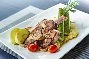 A gourmet dish featuring grilled meat, vegetables, and garnishes on a white plate.