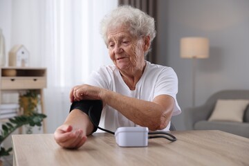Senior woman measuring blood pressure at wooden table indoors