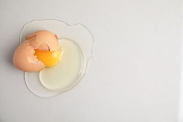 Broken raw egg with shell on light grey background, top view. Space for text