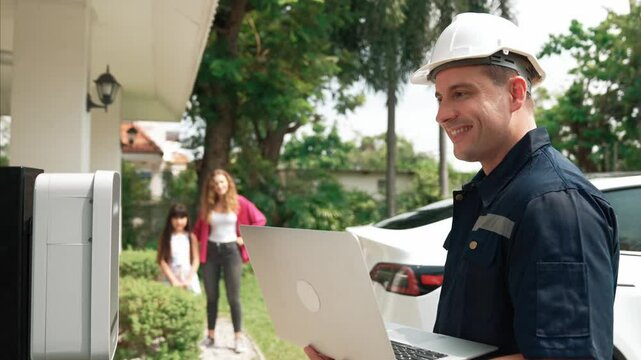 Qualified technician working on home EV charging station installation, making troubleshooting and configuration setup on charging system with laptop for EV at home. Fastidious