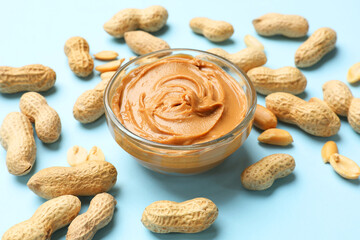 Tasty peanut butter in bowl and groundnuts on light blue background, closeup