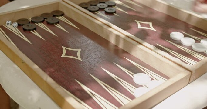 A detailed view of a person playing backgammon outdoors, capturing the movement of the game pieces on a wooden board.