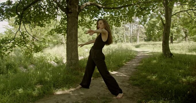 A carefree young woman performs an interpretive dance in nature, expressing herself through movement and nature.