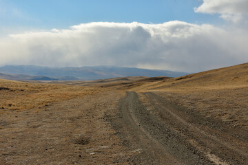 The field road rises to a high hill illuminated by the rays of the autumn sun through cumulus clouds.