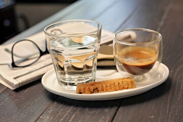 A coffee and water setup on a table, accompanied by a newspaper and glasses.