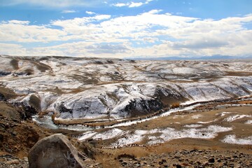A scenic landscape featuring rolling hills, a winding river, and a partly cloudy sky.