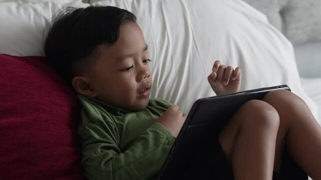 Little boy is smiling while playing with digital tablet at home. Modern kid and education technology.