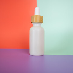 White oil dropper bottle with a bright color block background with hand lifting lid