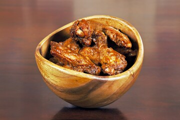A wooden bowl filled with deliciously glazed chicken wings.