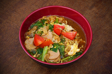 Indonesian Mie Tek-Tek noodle soup with vegetables and meat served in red bowl on wooden table. Food concept.