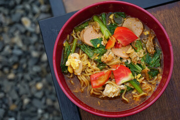 Indonesian Mie Tek-Tek noodle soup with vegetables and meat served in red bowl on wooden table. Food concept.