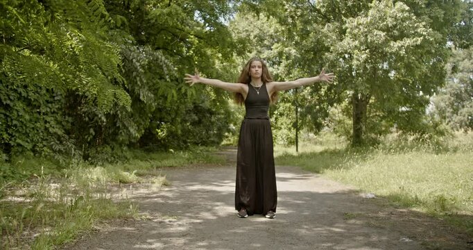 Young woman performs interpretive dance moves in a sunny park, expressing freedom and joy through movement.