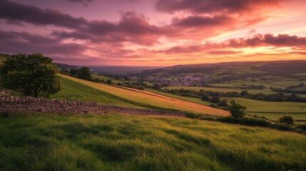 Obraz premium A rural landscape with a vibrant sunset sky, green fields, and a distant village on the horizon, offering a calm and peaceful backdrop