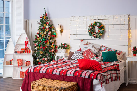 Interior of festive bedroom with comfortable bed and Christmas tree. checkered blanket. Christmas home decoration. Christmas tree, garland with lights, gifts. Winter holidays